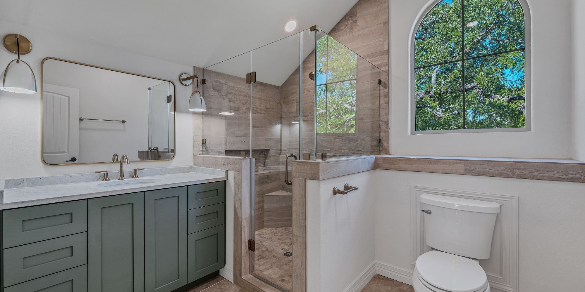 Elegant bathroom remodel in San Antonio with natural stone tile shower and brushed gold fixtures by Hill Haven Homes
