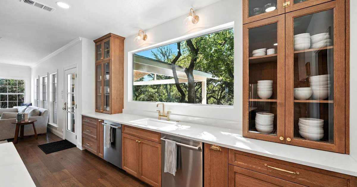 Bright San Antonio kitchen by Hill Haven Homes featuring custom wood cabinetry, brass fixtures, and large picture window