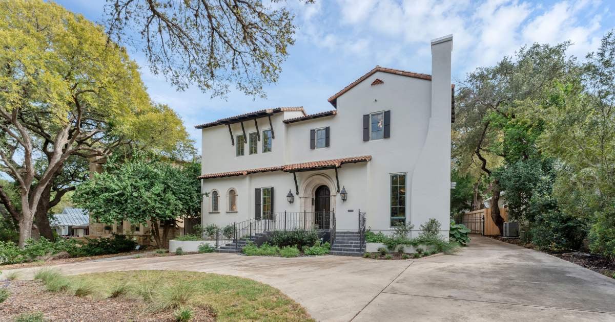 Exterior of a San Antonio custom home by Hill Haven Homes featuring stucco walls, clay roof tiles, and elegant wrought iron details