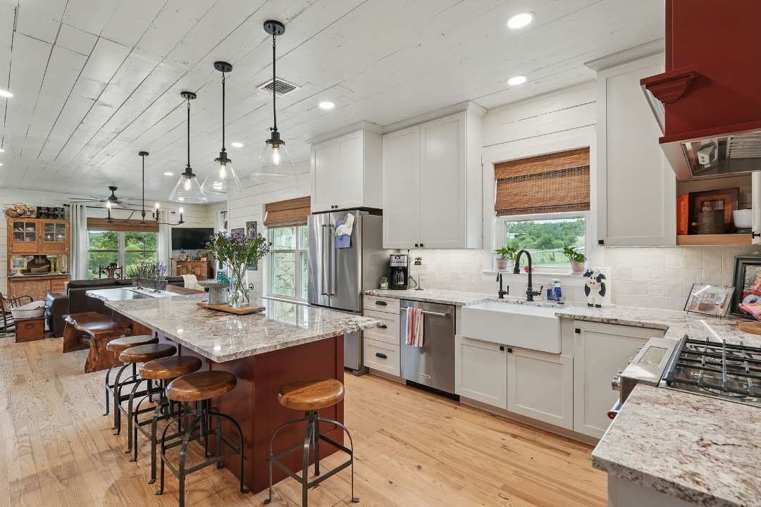 Farmhouse-style kitchen remodel with a large granite island, pendant lighting, and white shaker cabinets in San Antonio home