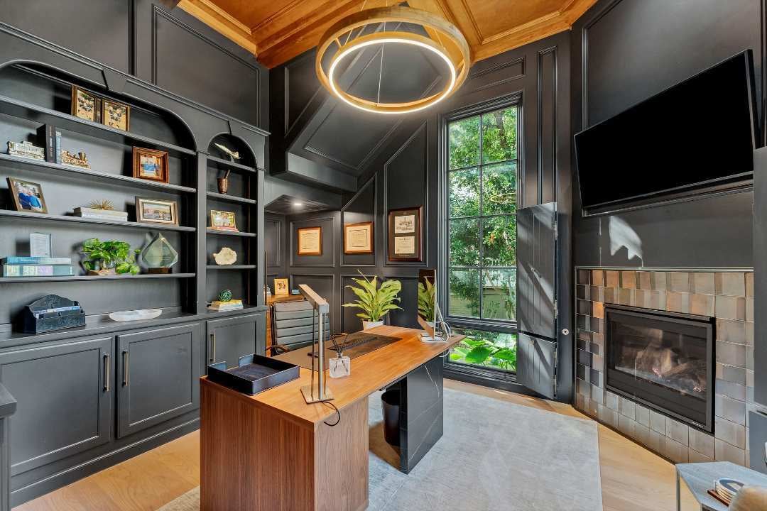 Sophisticated home office with black paneled walls, modern wood desk, built-in shelving, and fireplace in San Antonio remodel